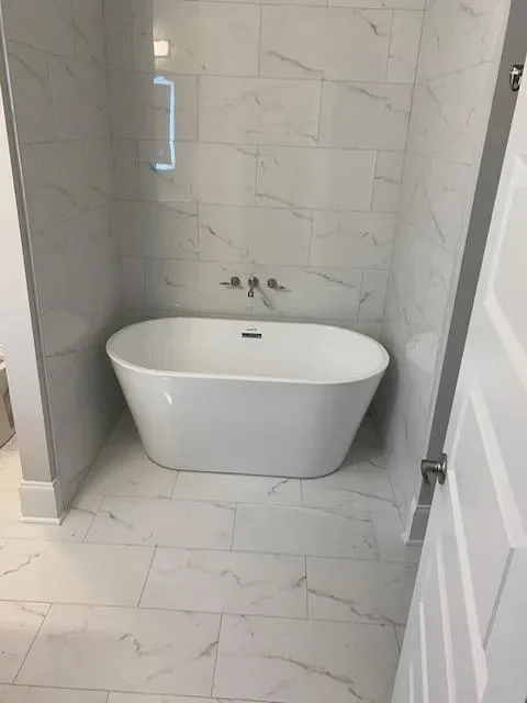 Modern white freestanding bathtub in marble-tiled bathroom with glass shower enclosure