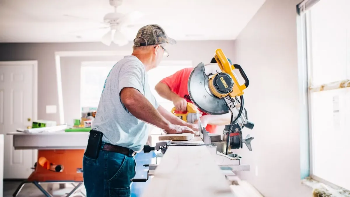 Two contractors operating a miter saw while cutting wood in a residential kitchen renovation