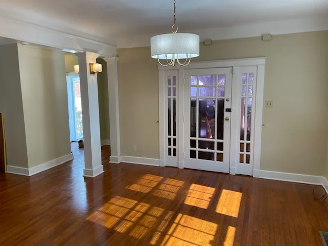 Empty living room with hardwood floors, white columns, pendant light, and glass French doors
