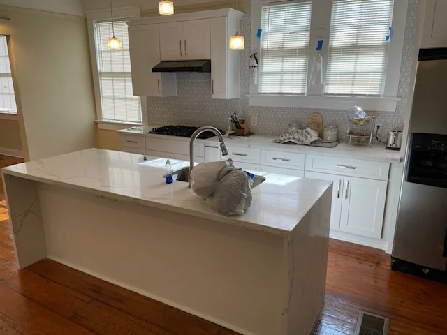 Modern white kitchen with island sink, stainless steel appliances, and hardwood floors
