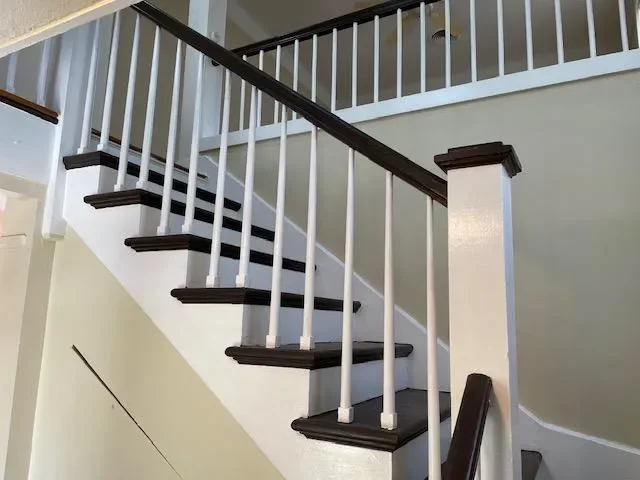 Modern staircase with white walls, dark wood steps, black handrail, and white metal balusters